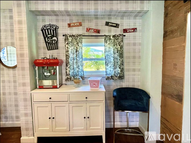 A white cabinet with a red popcorn machine on top and a black chair in front of it.
