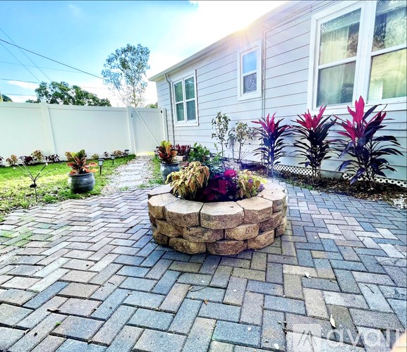 A backyard with a circular stone fire pit surrounded by a brick patio.