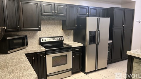 A kitchen with black cabinets and a stainless steel refrigerator.