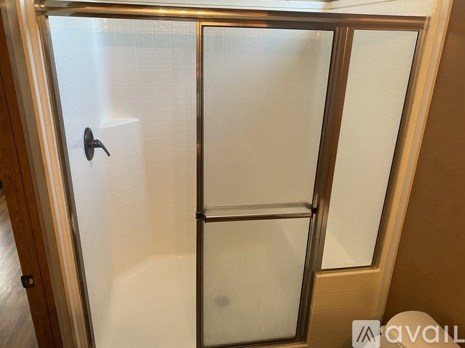 A shower with a glass door and a black handle.