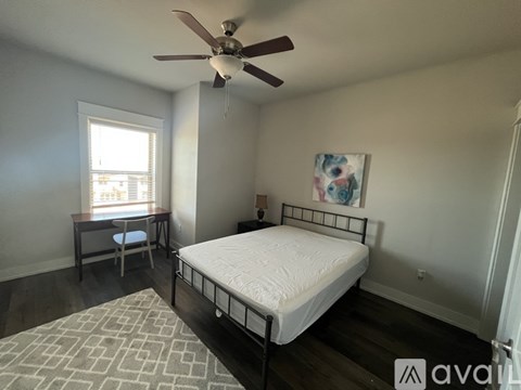 A bedroom with a bed, a table and a ceiling fan.