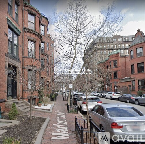 A street view of a residential area with parked cars and brick buildings.