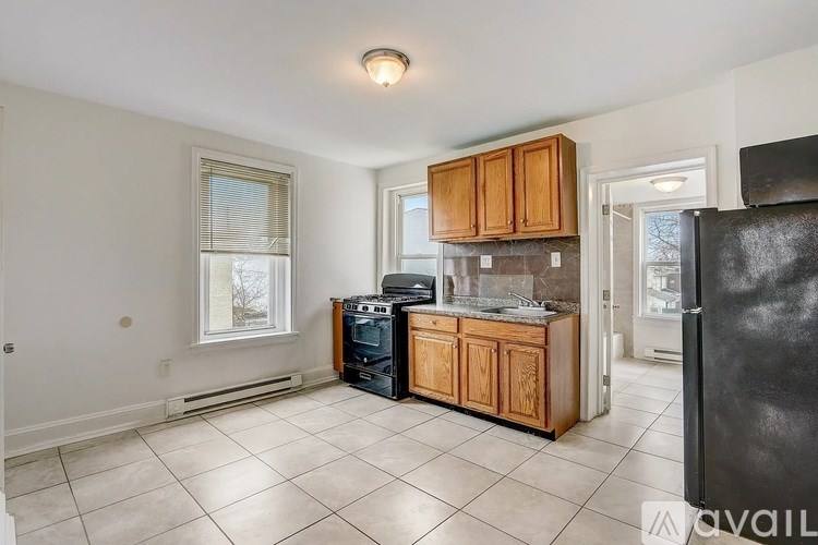 A kitchen with a black refrigerator, wooden cabinets, and a window with blinds.