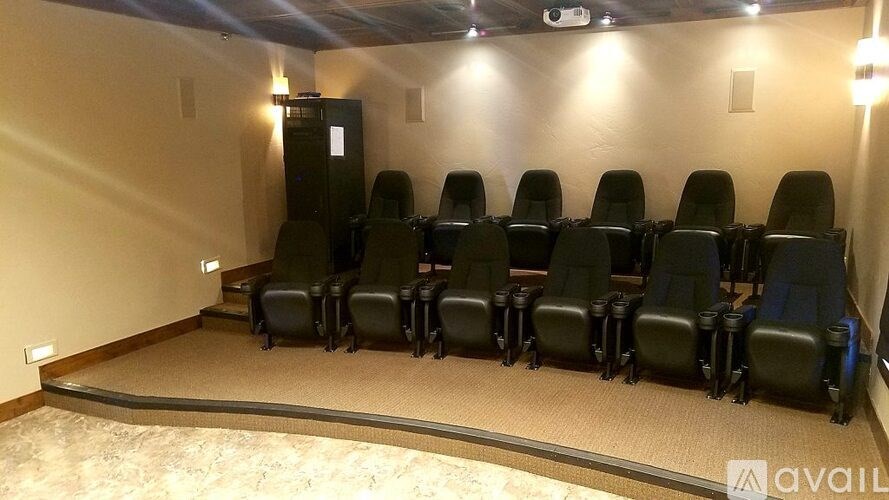 A row of black cinema seats are arranged in front of a screen.