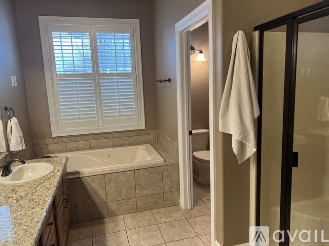 A bathroom with a tub, toilet, sink, and a window with shutters.