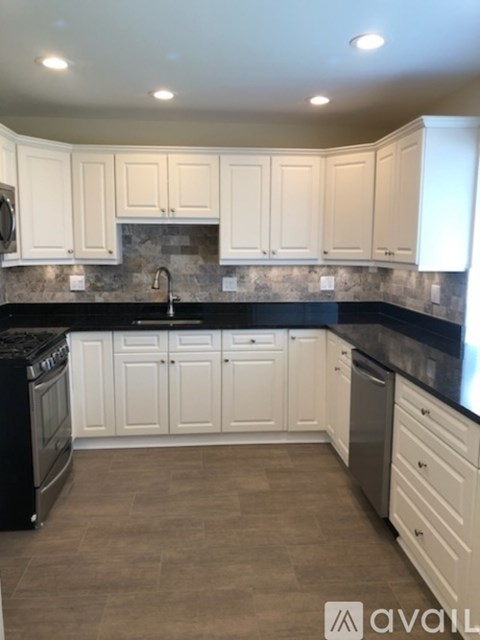 A kitchen with white cabinets and black countertops.