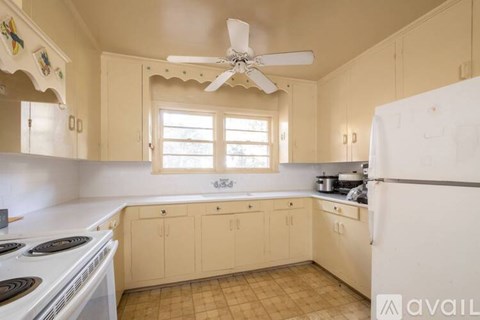 A kitchen with a white stove top oven, a white refrigerator, and a window with blinds.