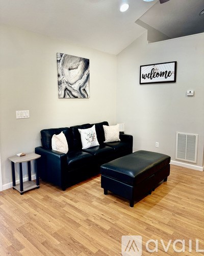 A black couch with a white pillow and a black ottoman in a room with wooden flooring.