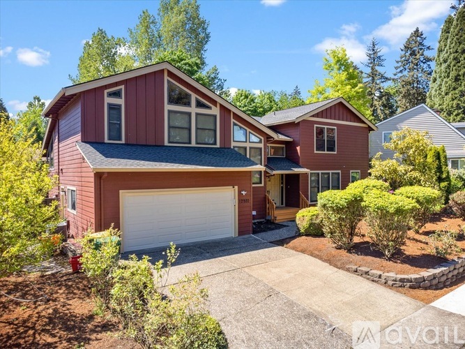 A red house with a white garage door is surrounded by greenery.