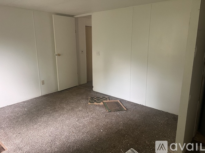 A room with white walls and a carpeted floor with a doorway leading to another room.