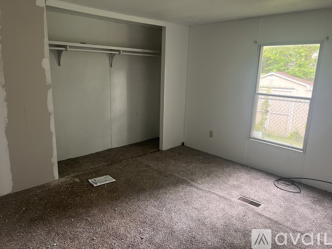 A room with a carpeted floor and a window showing a fence outside.