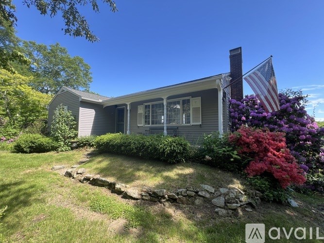 A house with a flag on the front and a garden with purple flowers.