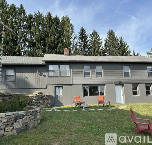 A house with a stone wall and two red chairs in front.