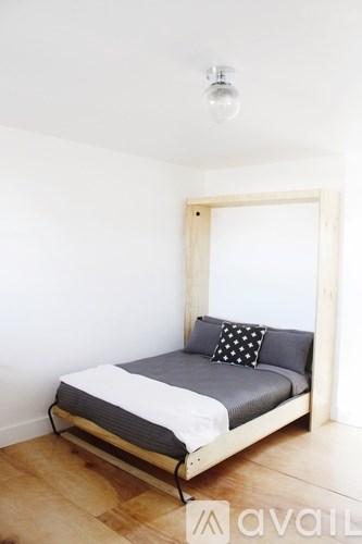 A bed with a grey pillow and a white sheet is in a room with wooden floors.