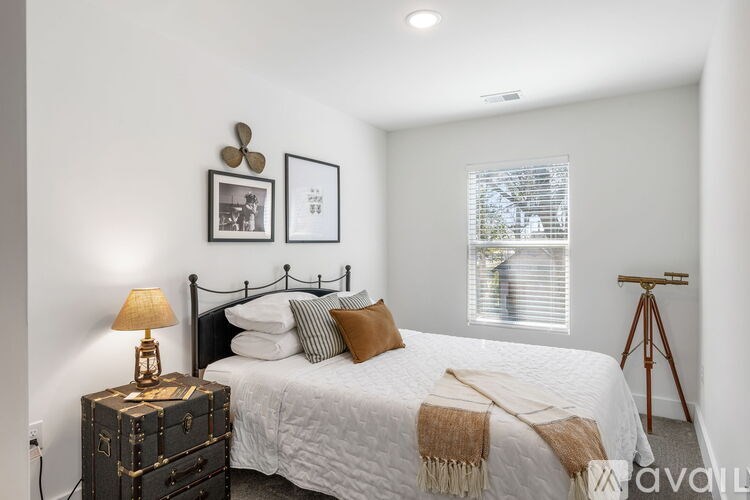 A bedroom with a bed, a lamp, a trunk, and pictures on the wall.