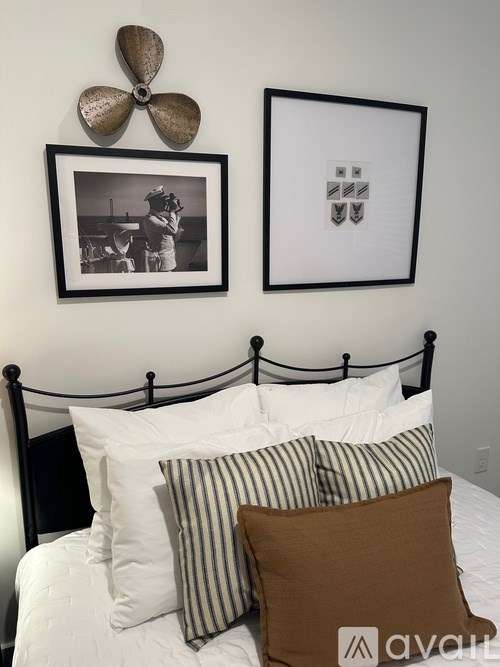 A bed with a white comforter and striped pillows with a fan and picture on the wall.