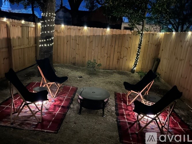 A backyard with a fence, chairs, and a table is set up for an evening outdoor gathering.