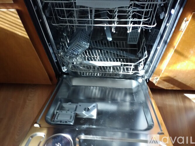 A Samsung dishwasher is open, showing the bottom rack and the dish drainer.