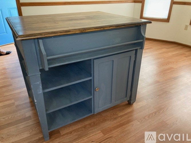 A blue wooden cabinet with a wooden top and a door is in a room with wooden flooring.
