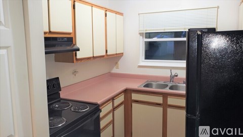 A kitchen with a black fridge, black stove, and a pink counter.