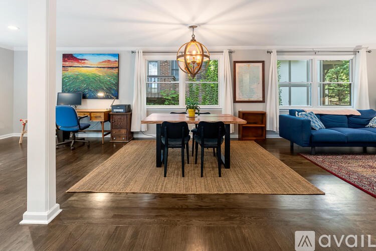 A well-lit room with a dining table and chairs, a couch, and a painting on the wall.