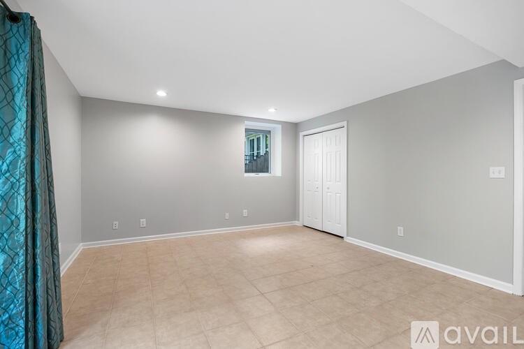 A spacious room with beige carpeting and a window with a view of a balcony.
