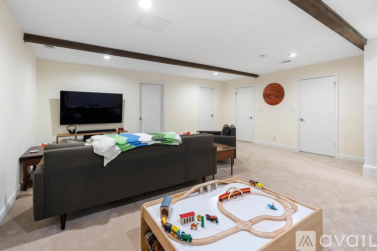 A living room with a grey couch, a wooden coffee table, a toy train set on a table, and a television.