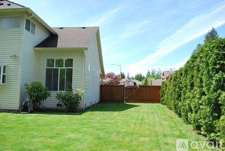 A house with a white exterior and a brown roof is surrounded by a green lawn and a hedge.