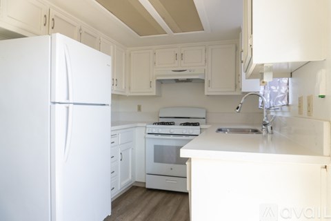 A white kitchen with a refrigerator, stove, and sink.