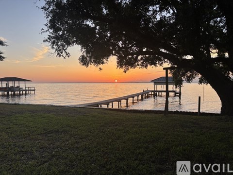A serene lakeside scene with a dock and a tree in the foreground during sunset.