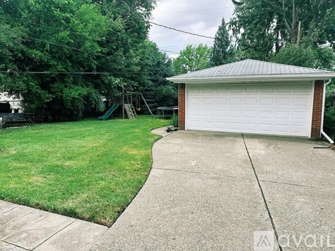 A detached garage with a white door is situated in a backyard with a green lawn and trees.