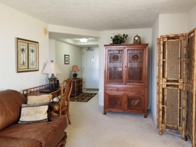A brown leather couch sits in a living room with a wooden cabinet and a chair.