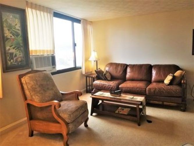 A brown leather couch sits in a living room with a wooden chair and coffee table.