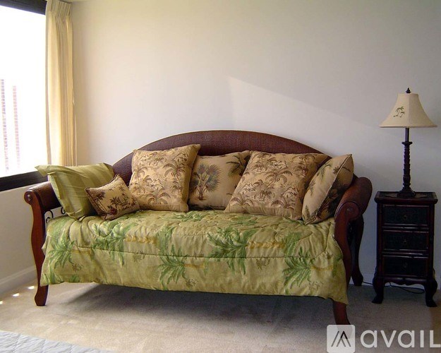 A green floral patterned sofa with a brown headboard and a lamp on a side table.