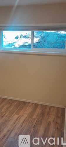 A room with wooden flooring and a window showing a blue sky.