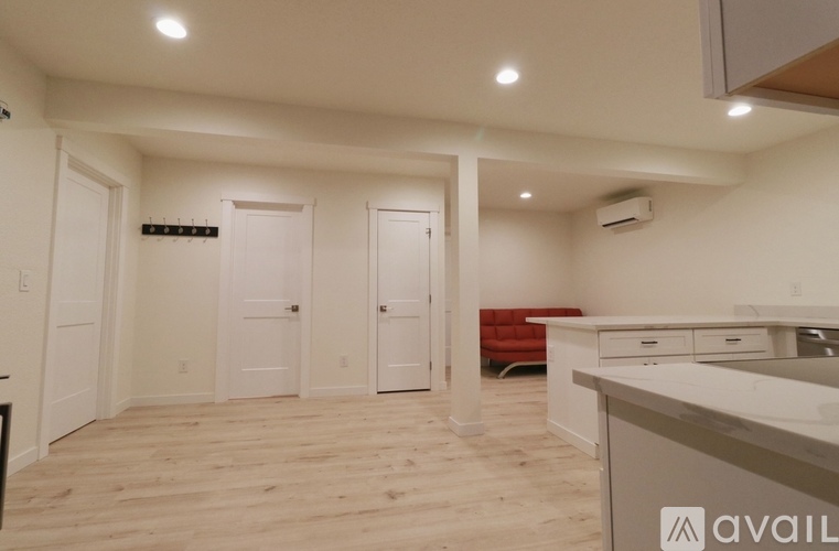 A room with a white ceiling and a wooden floor with a white counter and a red chair.