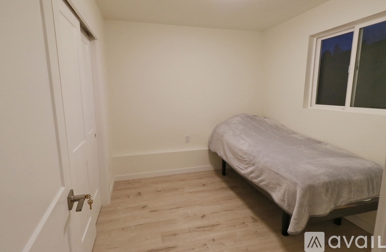 A bedroom with a bed, wooden floor, and a window with a white door.