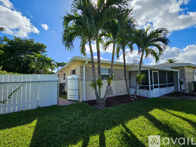 A house with a white fence and palm trees in front.