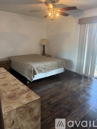 A bedroom with a bed, wooden floor, and a ceiling fan.