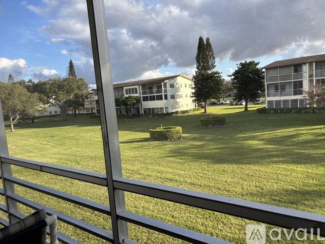 A view of a grassy area with trees and a building in the background from behind a fence.