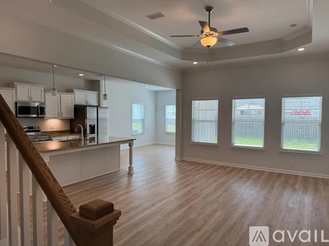 A spacious living room with a staircase on the left and a kitchen area with white cabinets and appliances on the right.