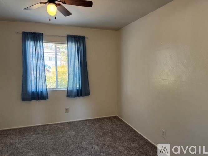 A room with a ceiling fan and a window with blue curtains.