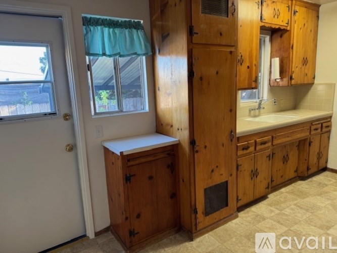 A kitchen with wooden cabinets and a window with a green curtain.