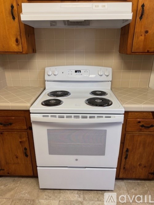 A white stove with four burners is in a kitchen with wooden cabinets.