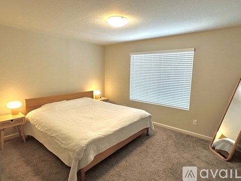 A bedroom with a bed, a nightstand with a lamp, a carpet, and a mirror.