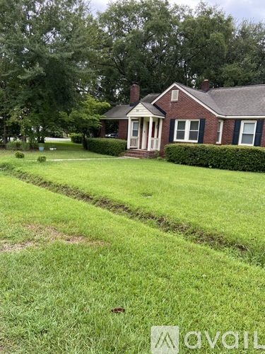 A house with a red brick exterior and a white door is surrounded by a well-manicured lawn.