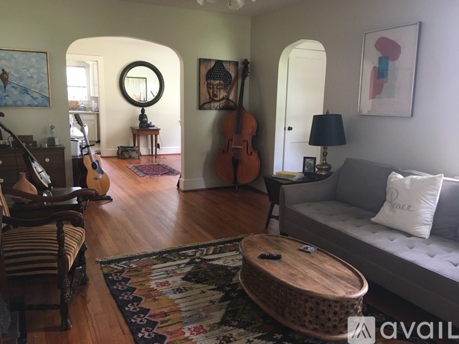 A living room with a couch, a guitar, a drum set, a violin, a mirror, and a rug.