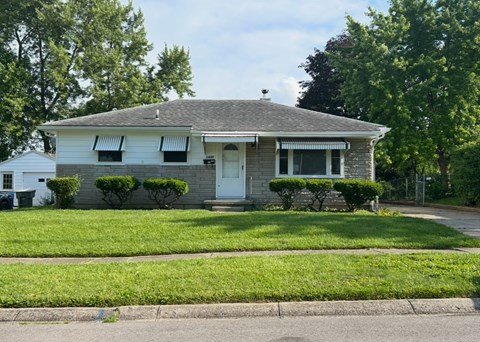 A house with a grey roof and white walls with green bushes in front.