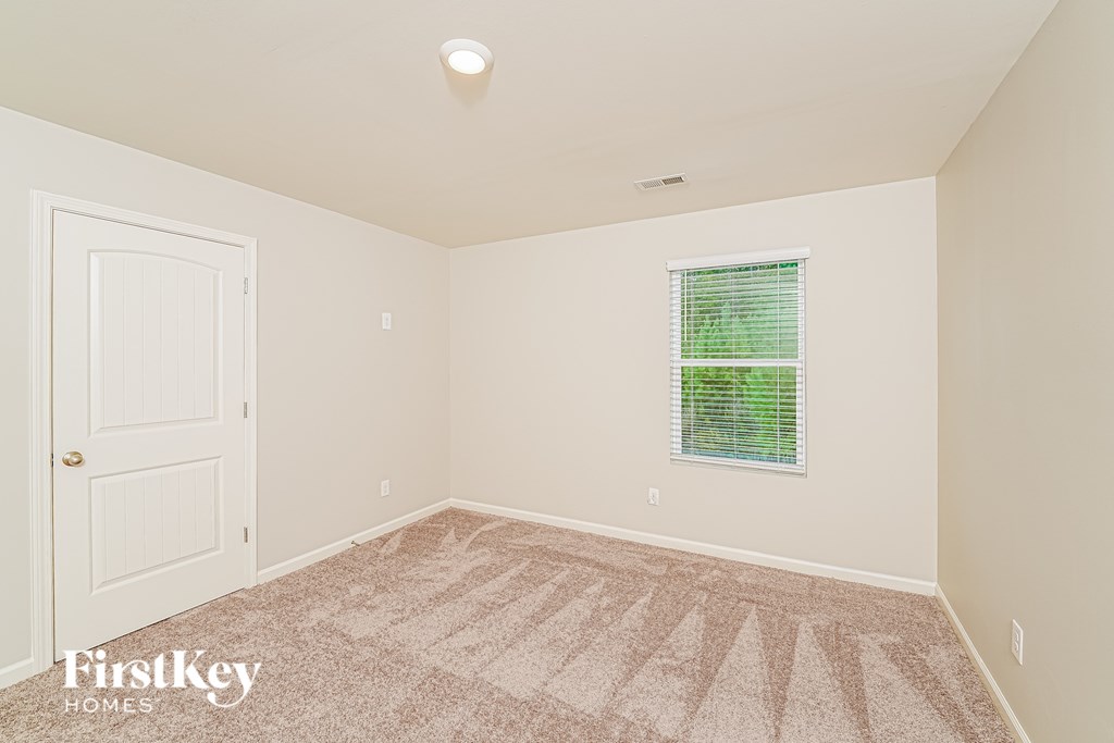 A room with a carpeted floor, a window with green blinds, and a white door.