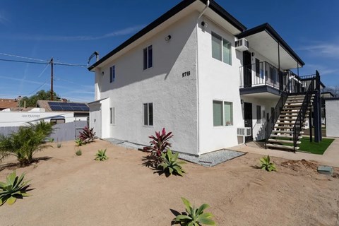 A white house with a black roof and a balcony on the second floor.